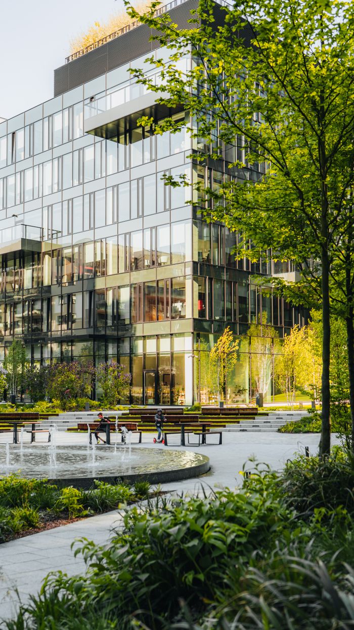 Spacious urban park surrounded by modern glass architecture with benches and fountain.